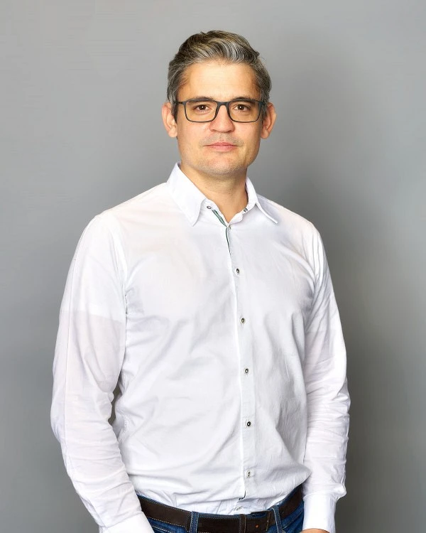 Dr. Stephan Zellner; -	Der zweite von den beiden Geschäftsführern trägt auch ein weißes Hemd, eine Brille und hat die Haare nach hinten gestylt.